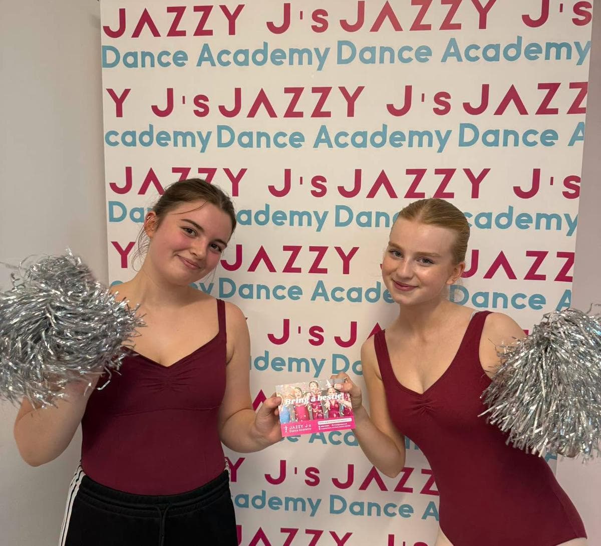 Two dancers with silver pom-poms in front of the Jazzy J's backdrop
