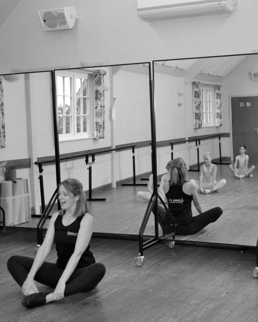 A teacher stretching with a pupil in front of the mirrors