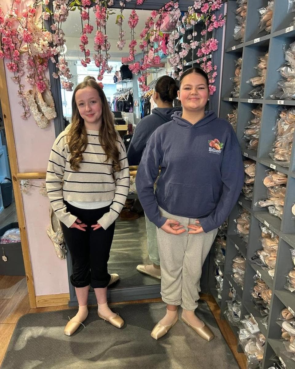 Two pupils posing by the pointe shoe wall