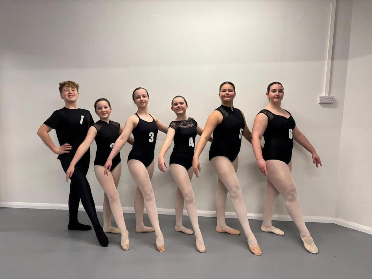 Five dancers in black leotards posing in the studio