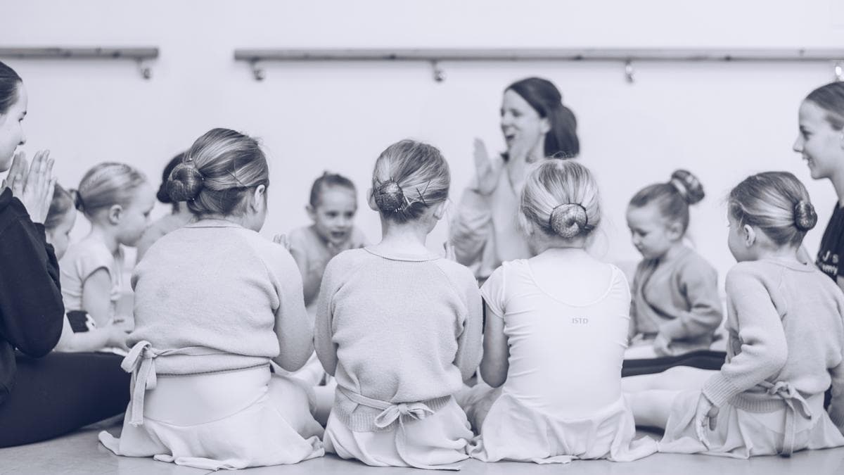 Young ballet pupils sitting in a circle listening to their teacher