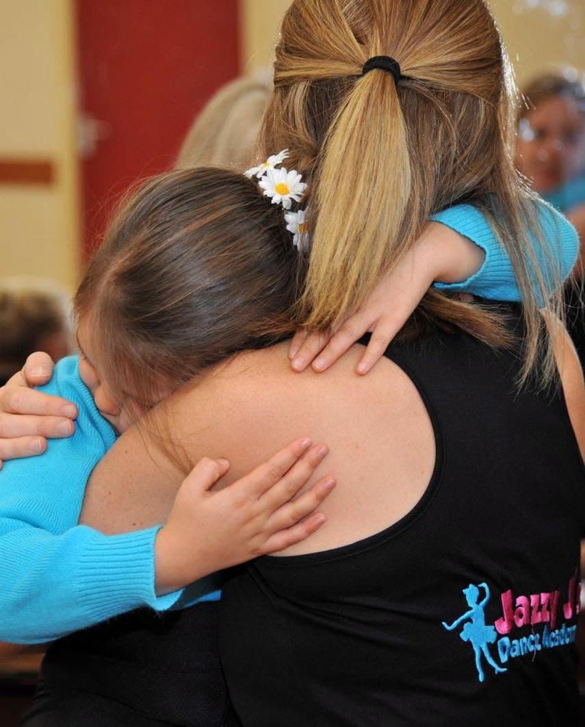 A young pupil hugging her teacher, who wears a Jazzy J's jacket