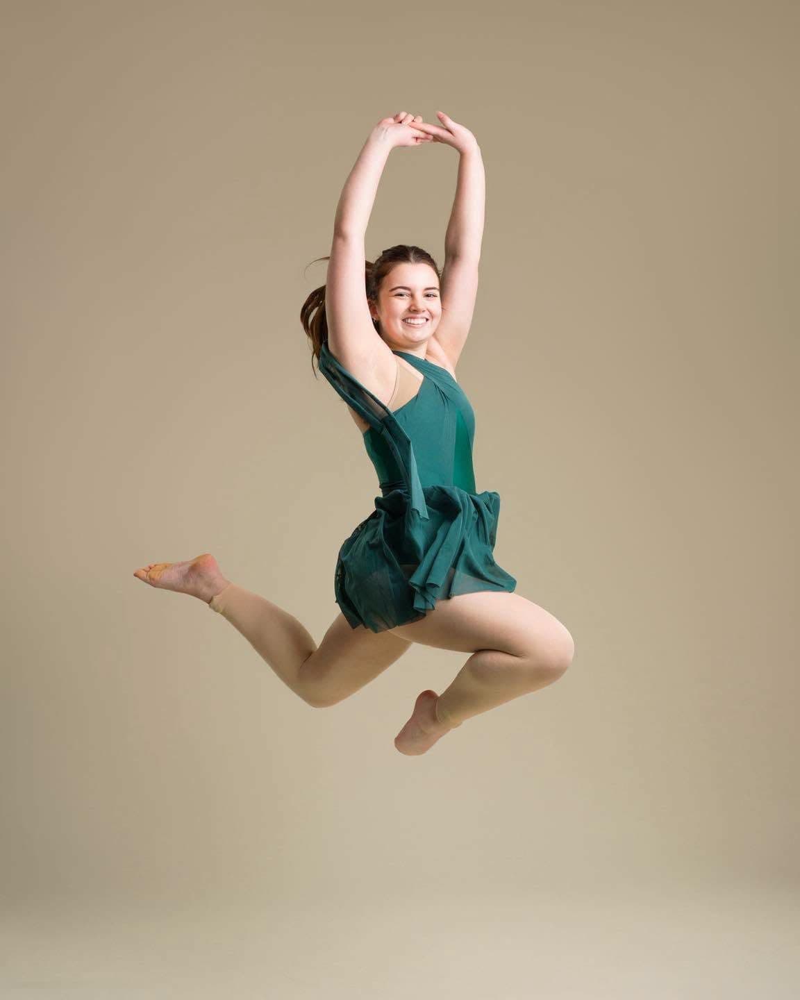 A dancer in a green dress mid-leap