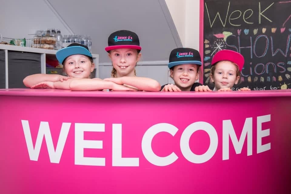 Children peeking over the pink Welcome reception desk